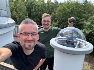 From left: Prof. Szymon Kozłowski (AOUW), Mateusz Żmija – coordinator of the Skytinel bolide network holding the Pułtusk meteorite. In the foreground, SN20 bolide camera. Photo by Szymon Kozłowski